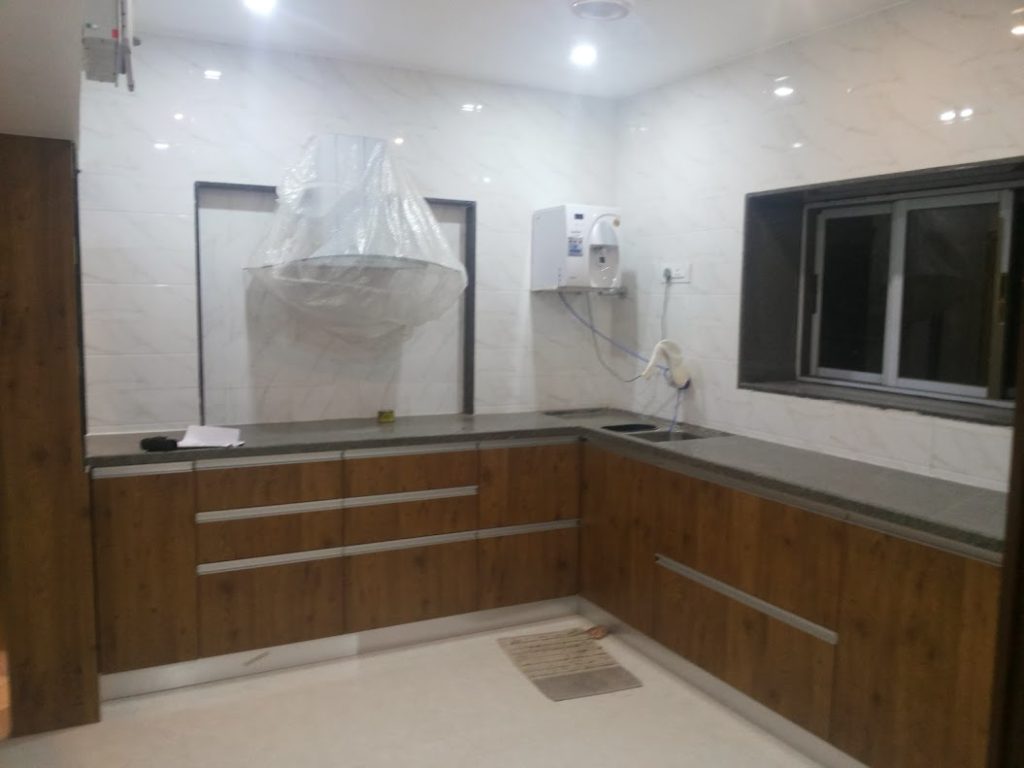 Chocolate-colored L-shaped modular kitchen with sleek cabinets and modern appliances.