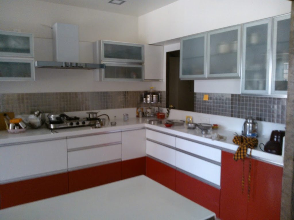 Red and white L-shaped modular kitchen design with modern finish.