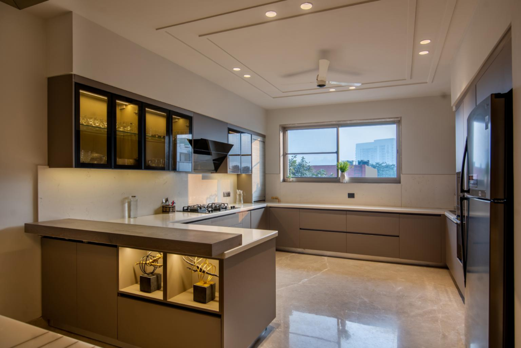 Modern, L-shaped kitchen with an island, beige lower cabinets, glass-front wall cabinets, and a large window overlooking buildings