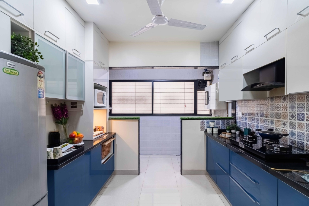 Narrow modern kitchen with white upper cabinets, blue lower cabinets, and a patterned tile backsplash along the right wall.