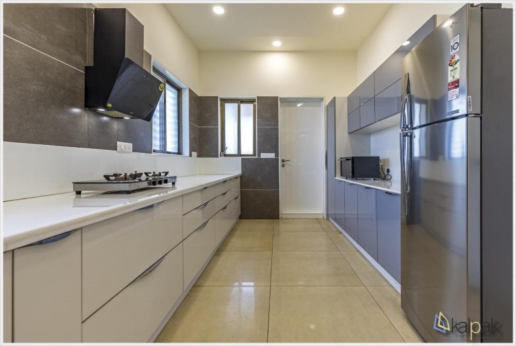 Modern galley kitchen with white countertops, gray lower cabinets, and a stainless steel refrigerator on the right side.